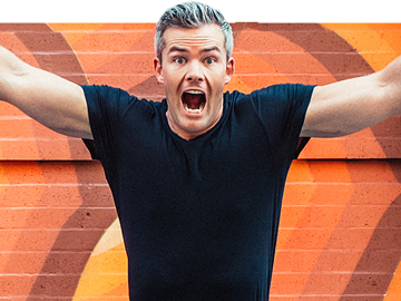 Close-up of Ryan Serhant jumping in front of colorful mural.
